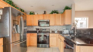 A modern kitchen with wooden cabinets, stainless steel appliances, and a black countertop. - Southern Dunes 1120 (Haines City)