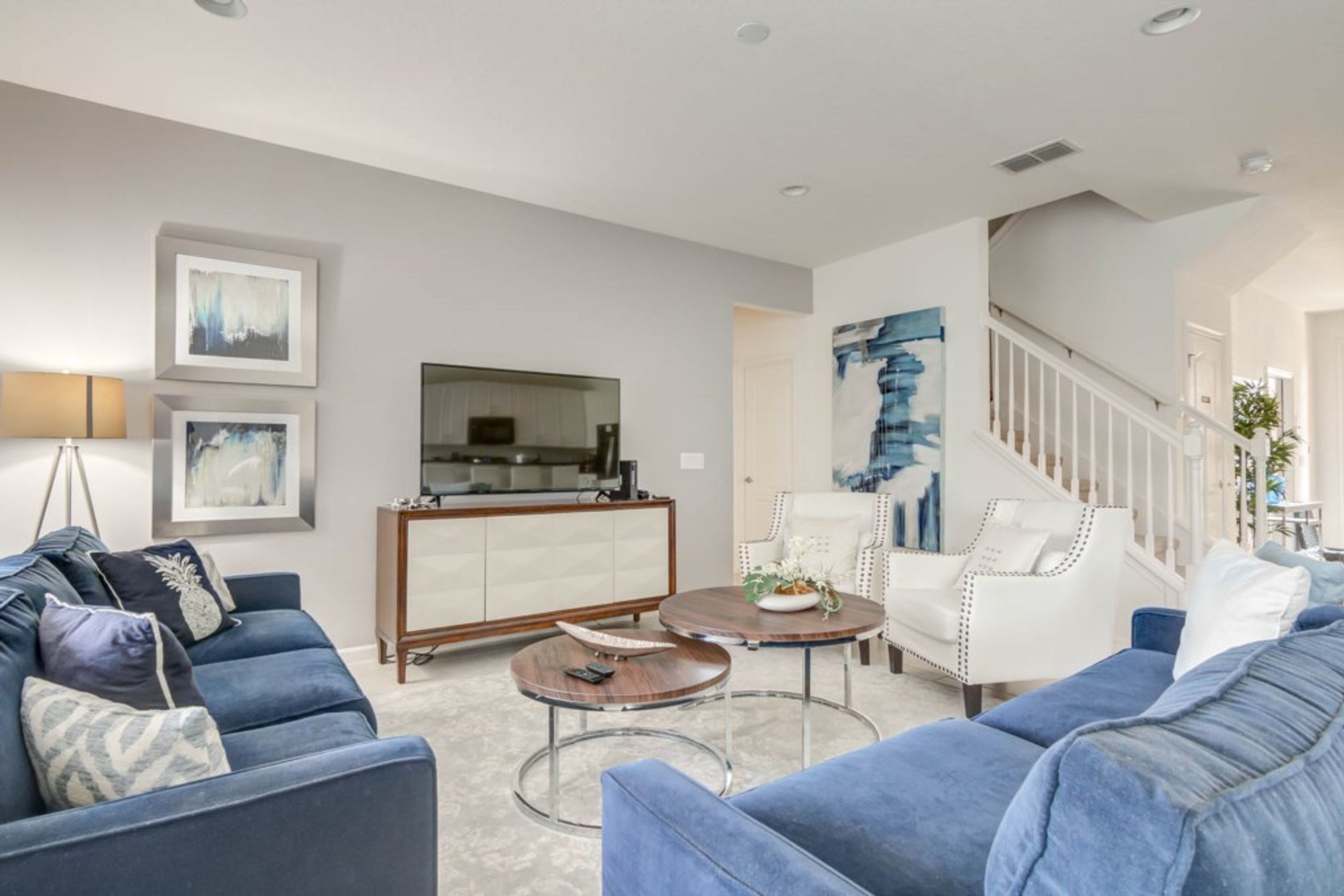 A modern living room with a blue sofa set, a wooden cabinet, and a white chair.