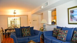 A living room with a blue sofa set, a glass coffee table, and a dining area with a table and chairs.