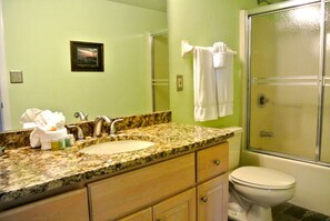 A bathroom with a granite countertop sink, a framed picture on the wall, a towel hanging on a rack, and a glass-enclosed shower.