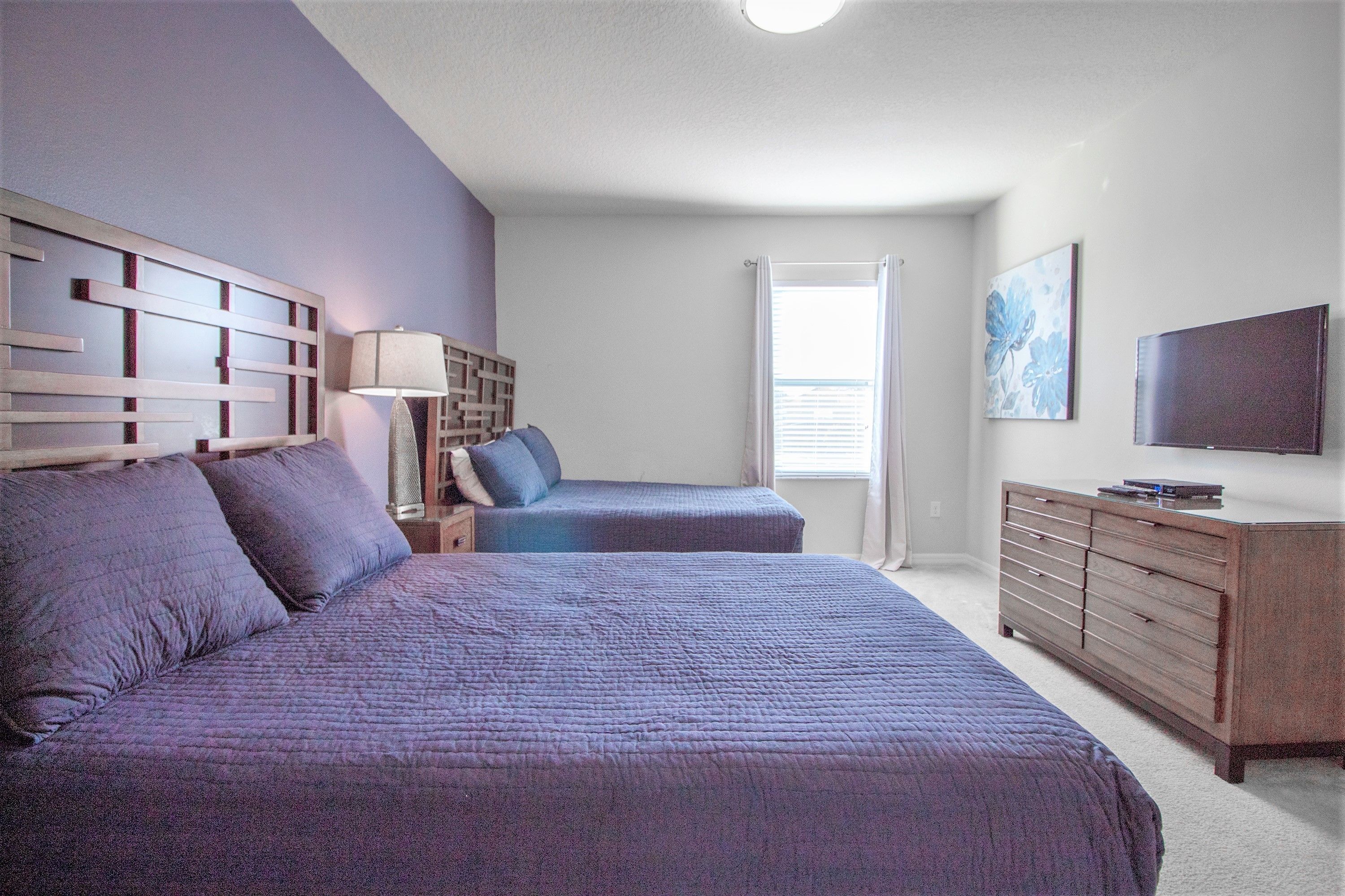A bedroom with two beds, a dresser, a TV, and a window with blinds.