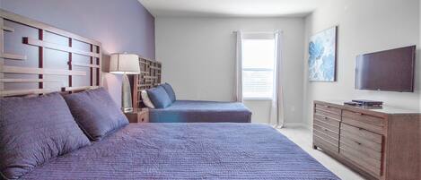 A bedroom with two beds, a dresser, a TV, and a window with blinds.