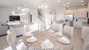 A modern kitchen with white cabinets, a stainless steel refrigerator, and a dining area with a wooden table set for six. - Golden Palms Vacation Resort 2580 (Kissimmee)