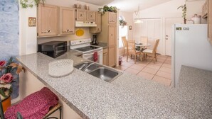 A kitchen with granite countertops, stainless steel appliances, wooden cabinets, and a dining area with a table and chairs. - Lindfields 2952 (Kissimmee)