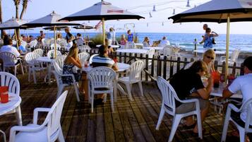 An outdoor dining area with white plastic chairs and tables, umbrellas, and a view of the ocean.