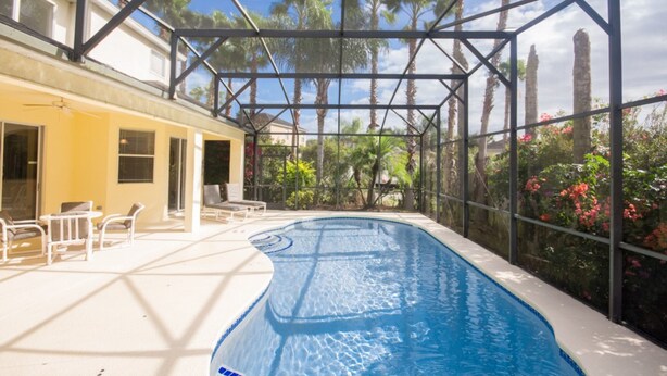 An indoor swimming pool with a glass ceiling, surrounded by chairs and a yellow building. - Calabay Parc 215 (Davenport)