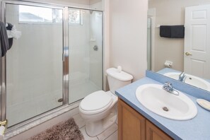 A bathroom with a glass-enclosed shower, a white toilet, a sink with a mirror, and a towel rack. - Calabay Parc 215 (Davenport)