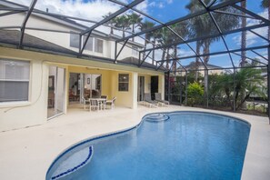 A swimming pool with a glass enclosure, surrounded by a patio area with chairs and a table. - Calabay Parc 215 (Davenport)