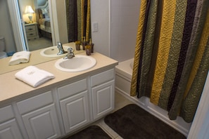 A bathroom with a sink, mirror, and bathtub. There are towels on the counter and a rug on the floor.