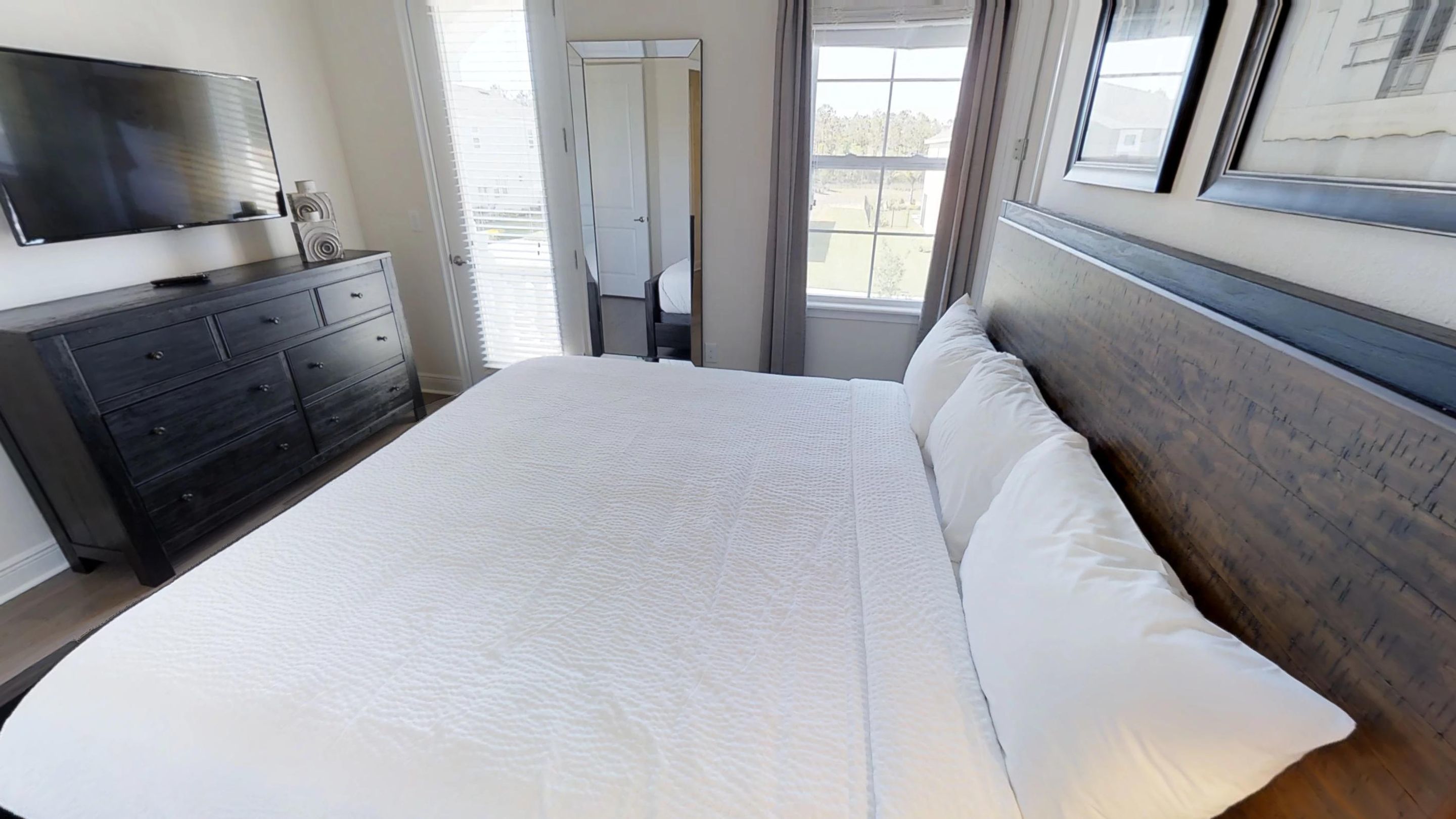 Quarto com uma cama grande, cômoda, televisão e janela com persianas.
