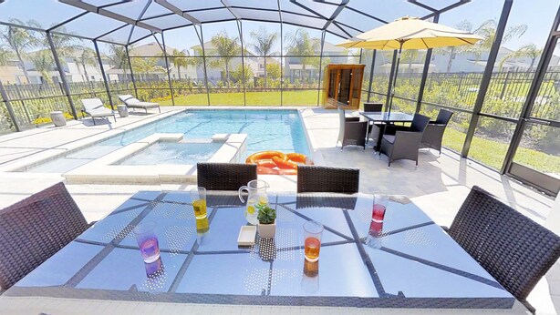 A covered outdoor area with a pool, lounge chairs, and tables with drinks. - Encore Resort at Reunion 7729 (Kissimmee)