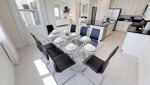 A modern kitchen with white cabinets, stainless steel appliances, and a dining area with a glass table and black chairs. - Encore Resort at Reunion 7729 (Kissimmee)
