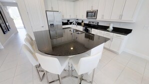 A modern kitchen with white cabinets, a stainless steel refrigerator, a microwave, and a granite countertop. - Encore Resort at Reunion 7729 (Kissimmee)