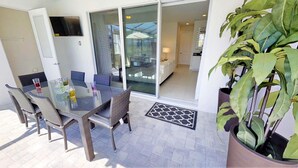 An outdoor dining area with a glass table and wicker chairs, a sliding glass door leading to a living area, and a large potted plant. - Encore Resort at Reunion 7729 (Kissimmee)