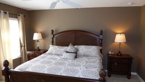 Un letto rifatto con una coperta a motivi, affiancato da due comodini con lampade, in una stanza con una testiera in legno e una ventola a soffitto.