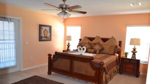 A bedroom with a bed, a ceiling fan, two bedside lamps, a nightstand, and a window with blinds.