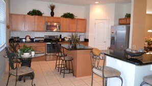 A modern kitchen with wooden cabinets, a central island, bar stools, and a refrigerator.