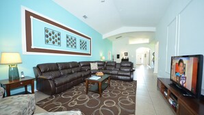 A living room with a brown leather sofa, a coffee table, and a TV on a wooden stand. - Crystal Cove 4718 (Kissimmee)