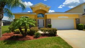 A yellow house with a garage, a palm tree, and a brick wall. - Crystal Cove 4718 (Kissimmee)