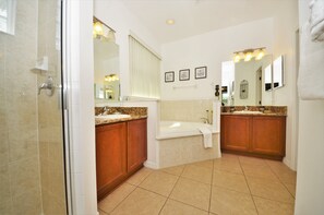 Ein Badezimmer mit Dusche, zwei Waschbecken, einer Badewanne und einem großen Spiegel.