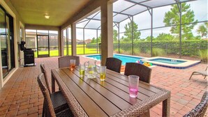 An outdoor patio with a table, chairs, and a pool in the background. - Champions Gate 9039 B (Davenport)