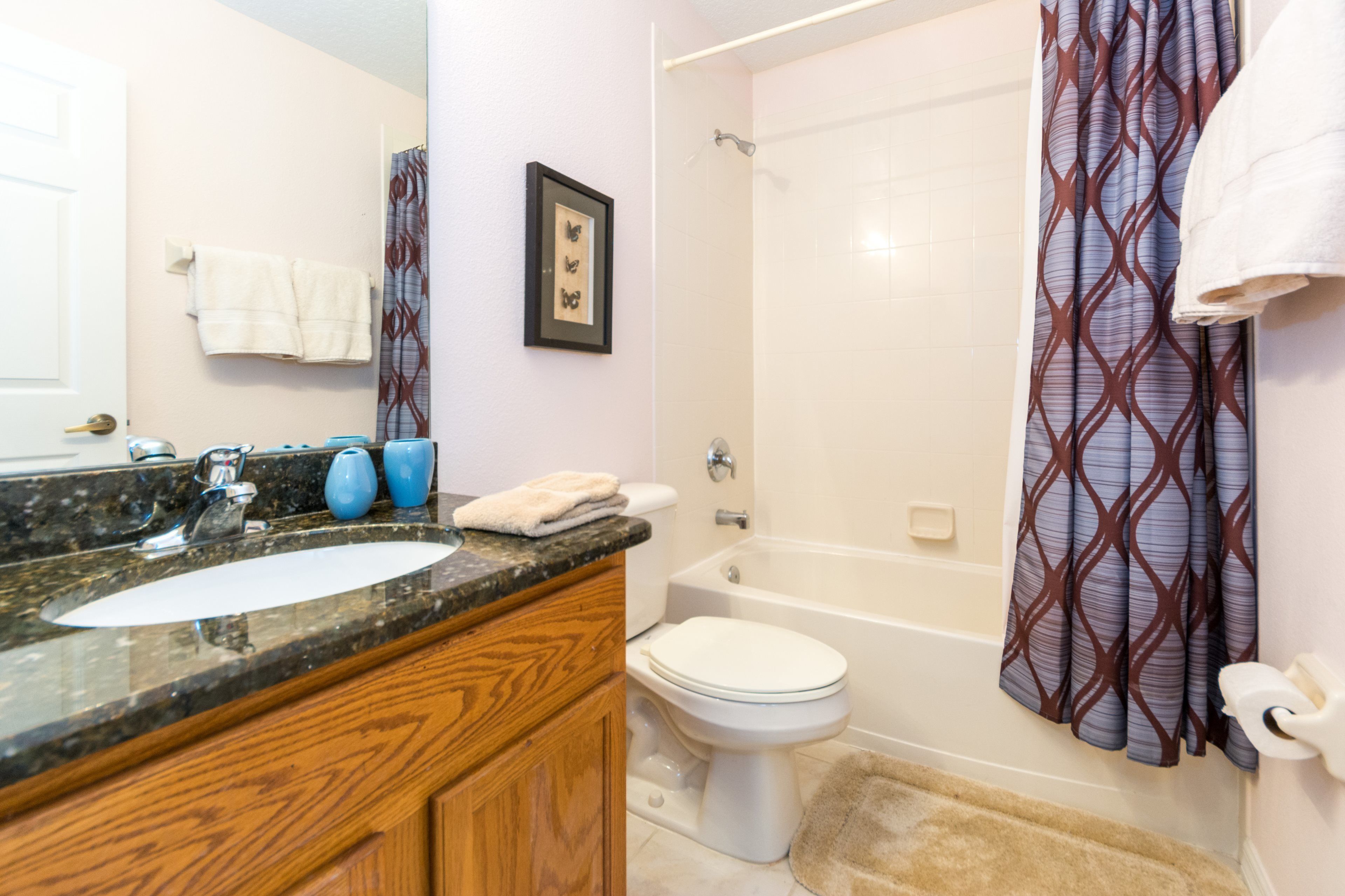 A bathroom with a marble sink, wooden vanity, white toilet, bathtub, and patterned shower curtain.