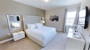 A hotel room with a large bed, a bedside table with a lamp, a mirror, and a flat-screen TV mounted on the wall. - Encore Resort at Reunion 7727 (Kissimmee)