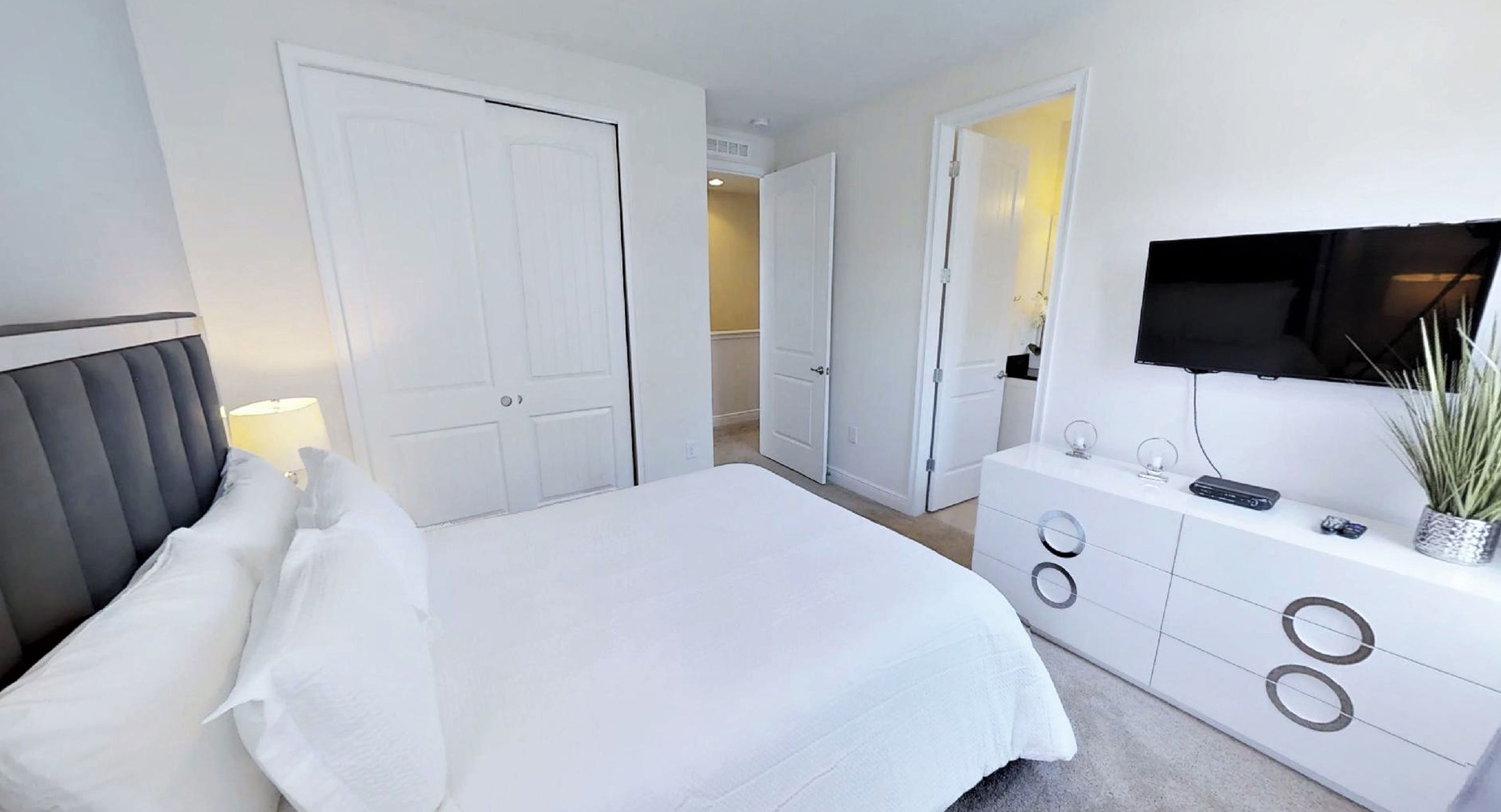 A modern bedroom with a bed, white wardrobe, and a TV mounted on the wall.