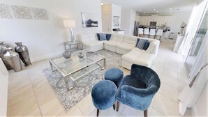 Un salon moderne avec une table basse en verre, deux fauteuils bleus, un canapé blanc et un tapis à motifs.