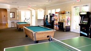Une table de billard, une table de ping-pong et des jeux d’arcade dans une pièce dotée d’arcades et offrant une vue sur la verdure environnante.