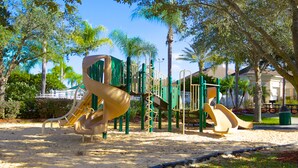 Une aire de jeux avec des toboggans et des structures d’escalade, entourée d’arbres et recouverte de sable.