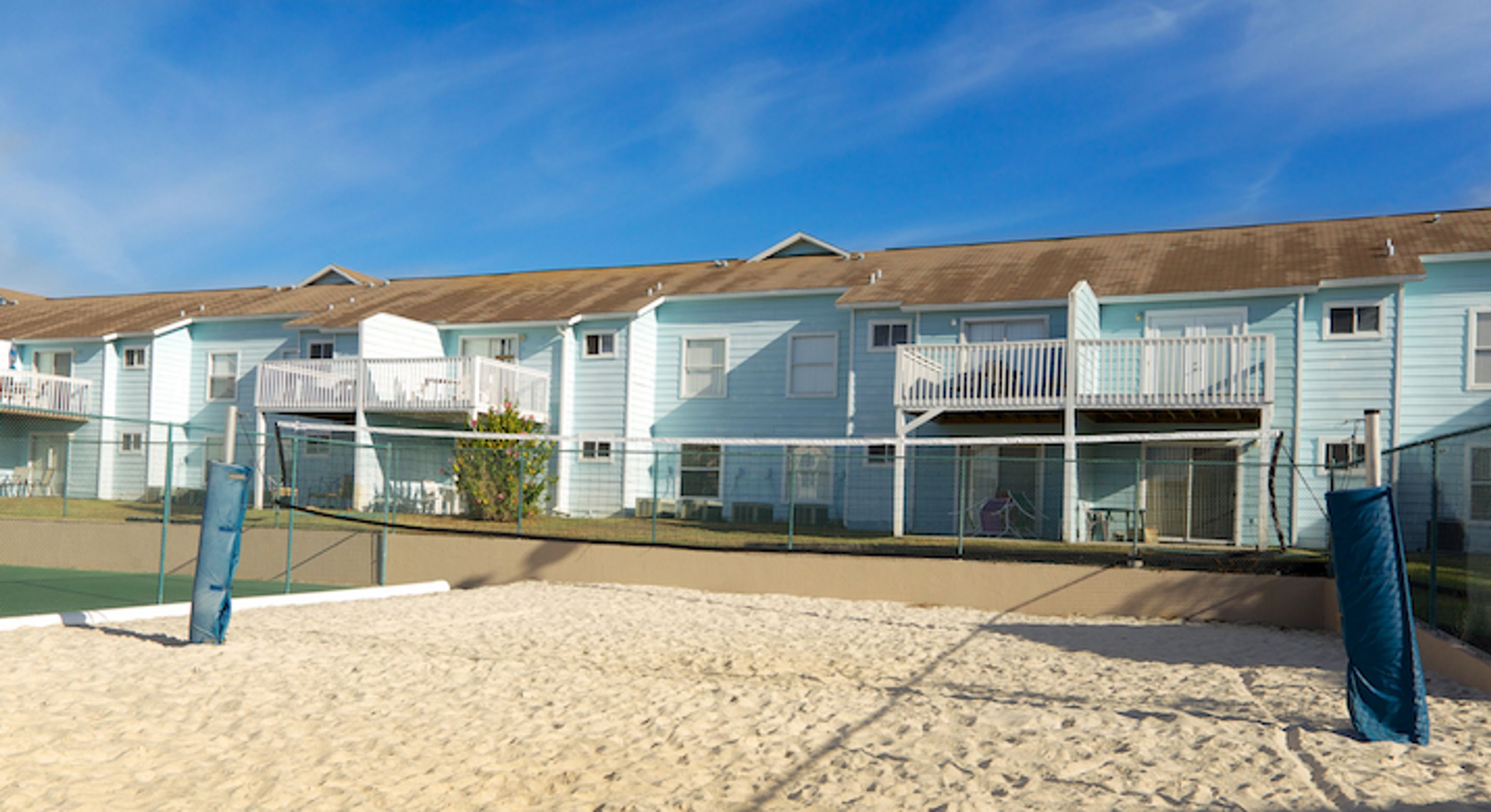 Uma fileira de casas de praia com varandas, uma praia arenosa e um céu azul límpido.