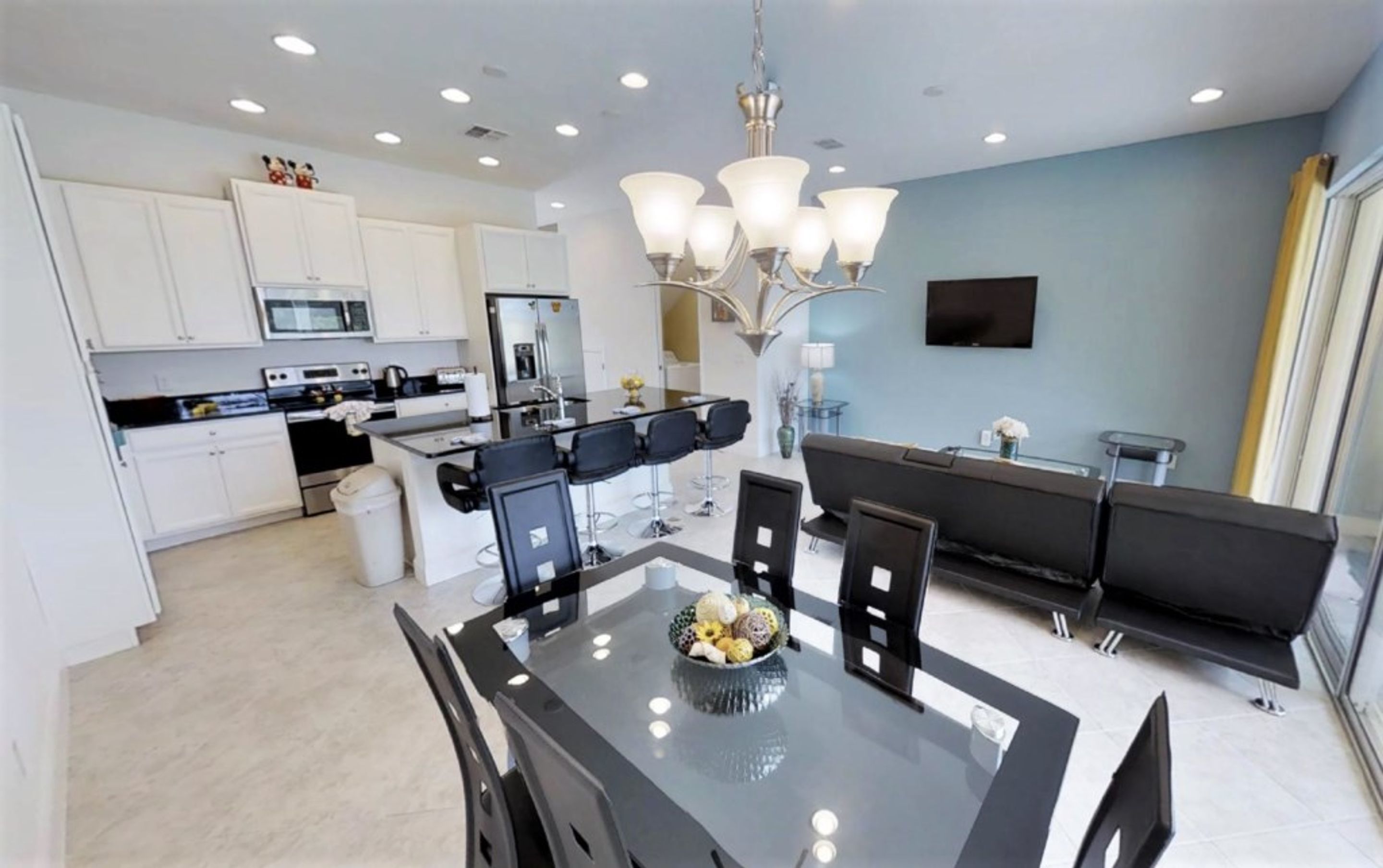 A modern kitchen with white cabinets, a dining area with a glass table, and a black sofa.