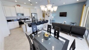 A modern kitchen with white cabinets, a dining area with a glass table, and a black sofa. - Festival Resort 220 (Davenport)