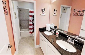 Casa de banho com duas pias, chuveiro com cortina do Mickey Mouse e decoração de parede com Mickey Mouse.