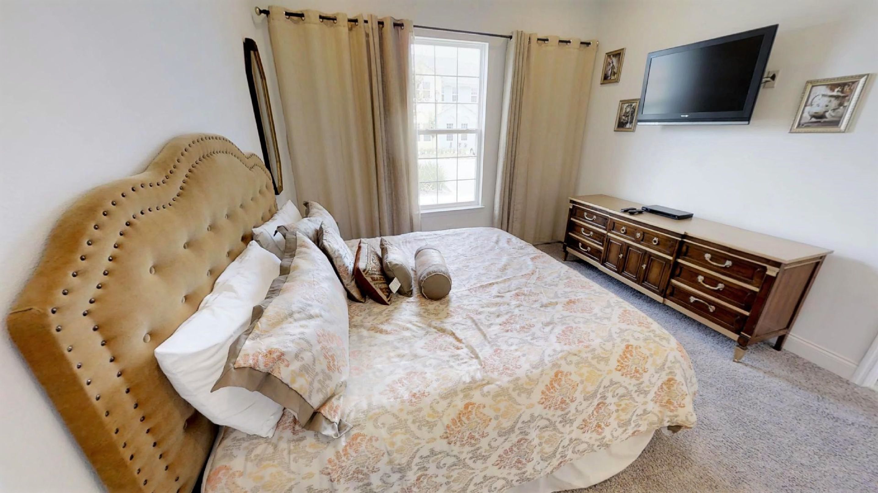 A bedroom with a large bed, a dresser, a television, and a window with curtains.