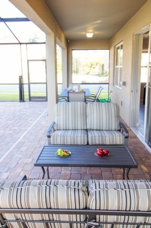 Relax in a stylish outdoor seating area with a sofa, armchair, and table, surrounded by a glass door and interlocking brick flooring.