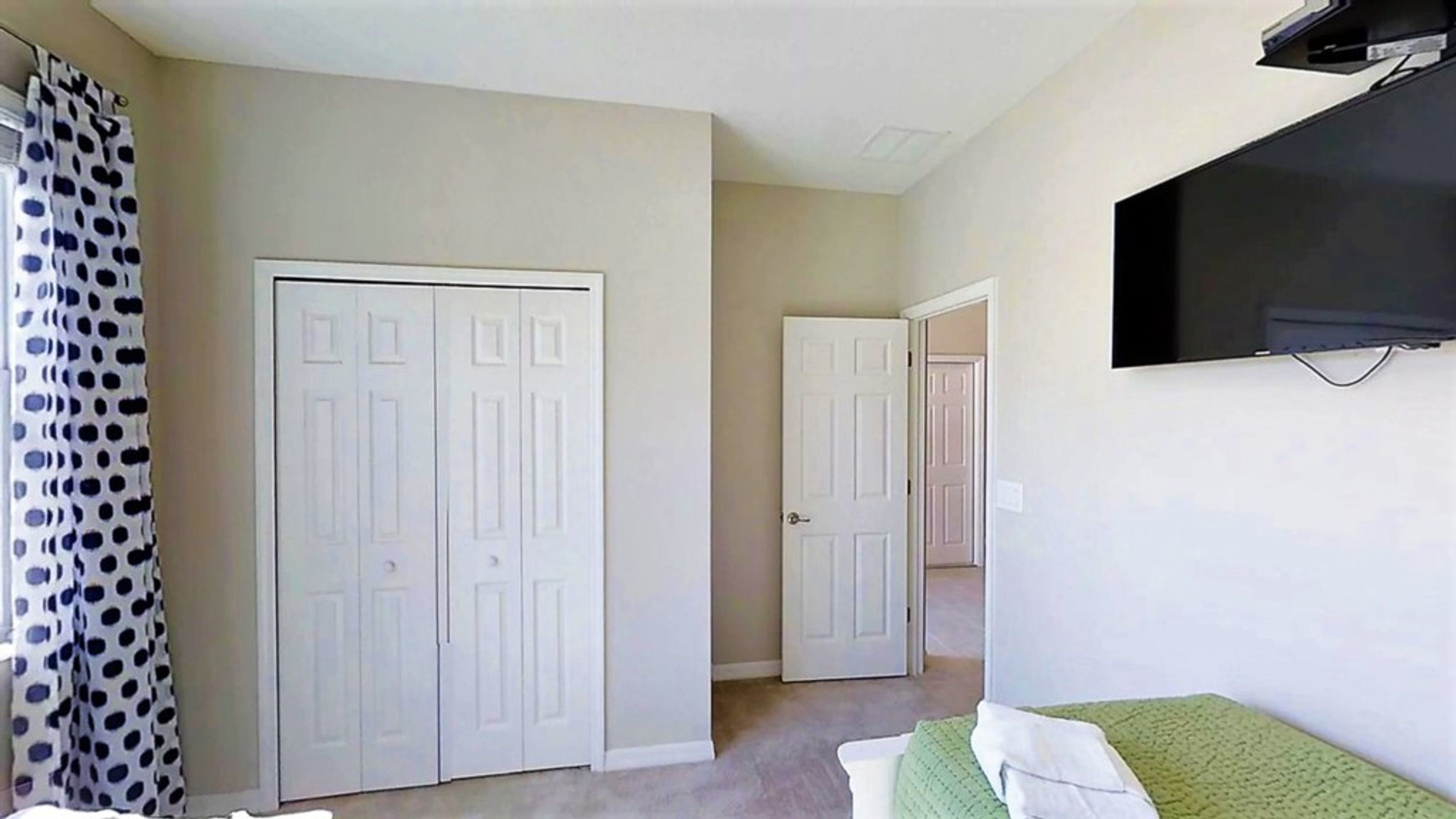 Una habitación con un armario grande, una cama con cubrecolcha verde y un televisor montado en la pared.