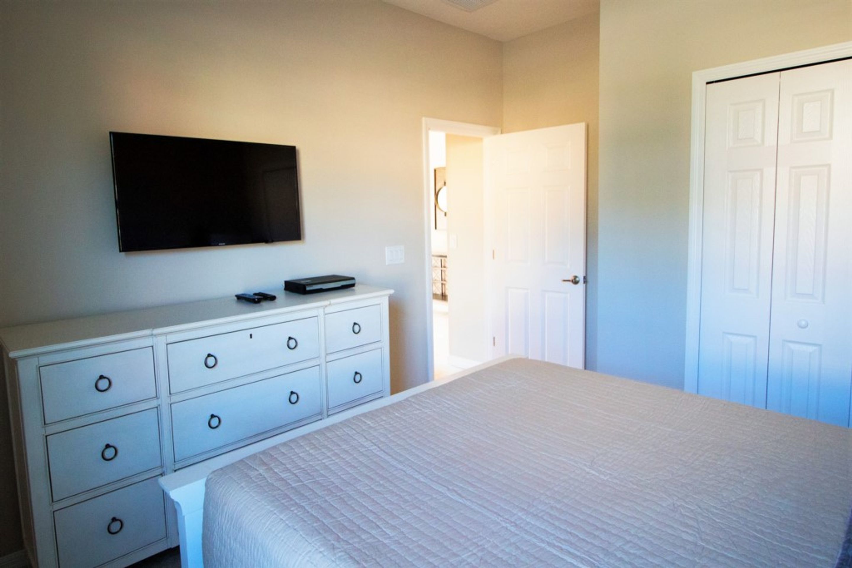 A bedroom with a bed, a dresser, a television, and a door.