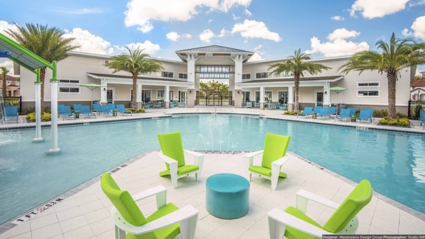 A pool area with lounge chairs and a building in the background. - Golden Palms Vacation Resort 24444 (Kissimmee)