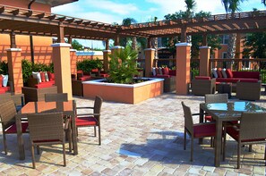 An outdoor patio area with wicker furniture, red cushions, and a central planter with greenery. - Regal Oaks 2776 (Kissimmee)