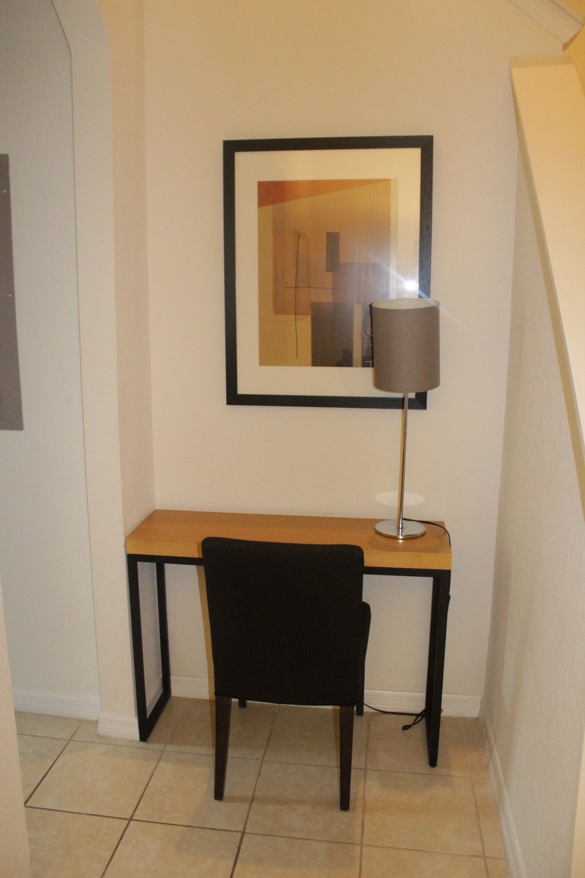 A small desk with a chair and a lamp in a corner of a room with tiled flooring.