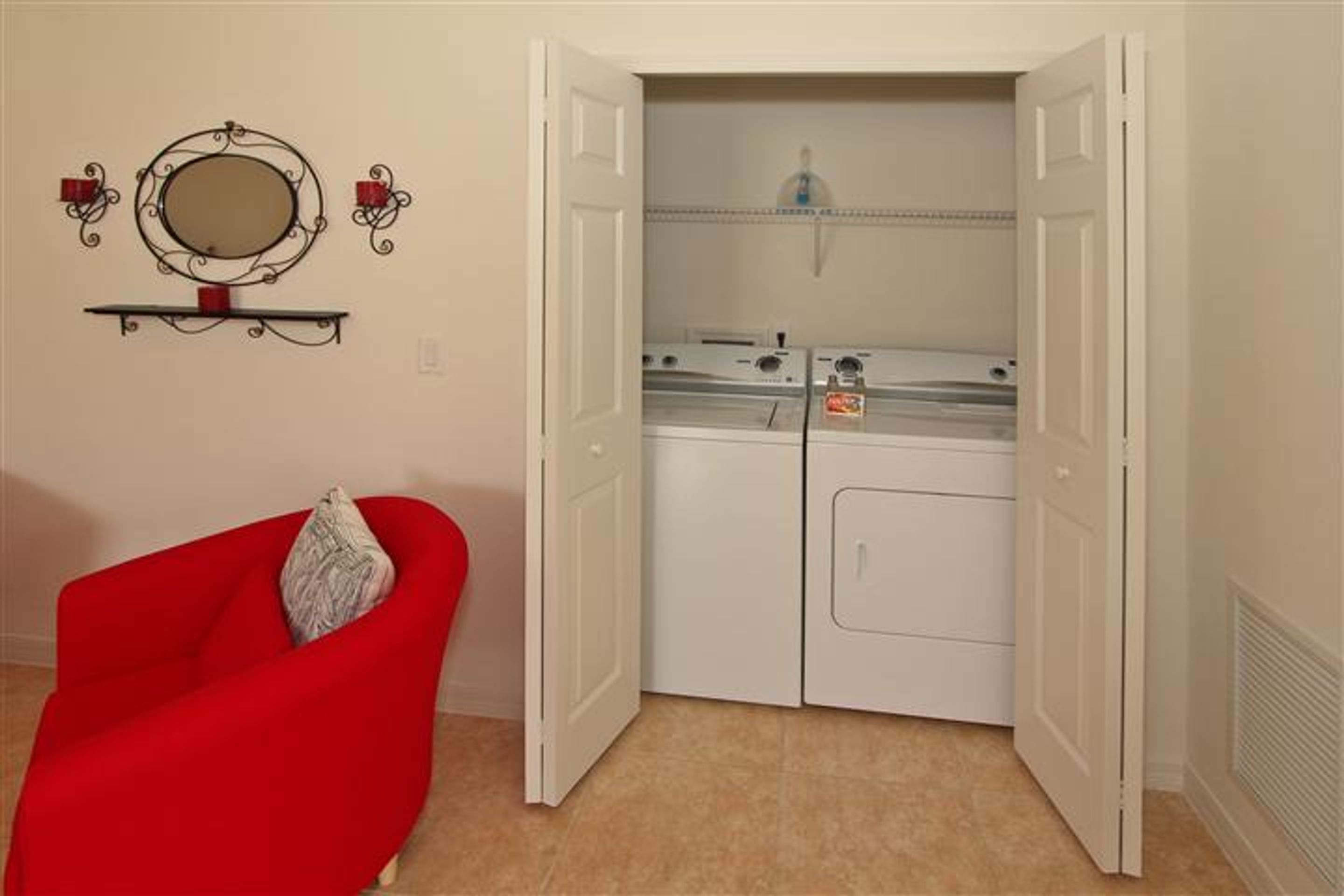 A laundry room with a red chair, a white door, and a wall-mounted mirror.