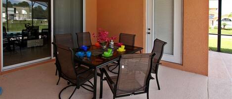 A covered patio with a table and chairs, a sliding glass door, and a view of the outdoors.