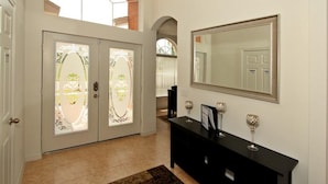 A hallway with a patterned rug, a black console table with decorative items, and a large mirror on the wall. - Crystal Cove 4725 (Kissimmee)