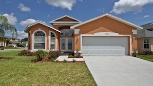 A two-story house with a garage, a well-maintained lawn, and a clear blue sky. - Crystal Cove 4725 (Kissimmee)