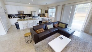A modern living room with a sectional sofa, a coffee table, and a dining area with a kitchen in the background. - Bella Vida 850 A (Kissimmee)