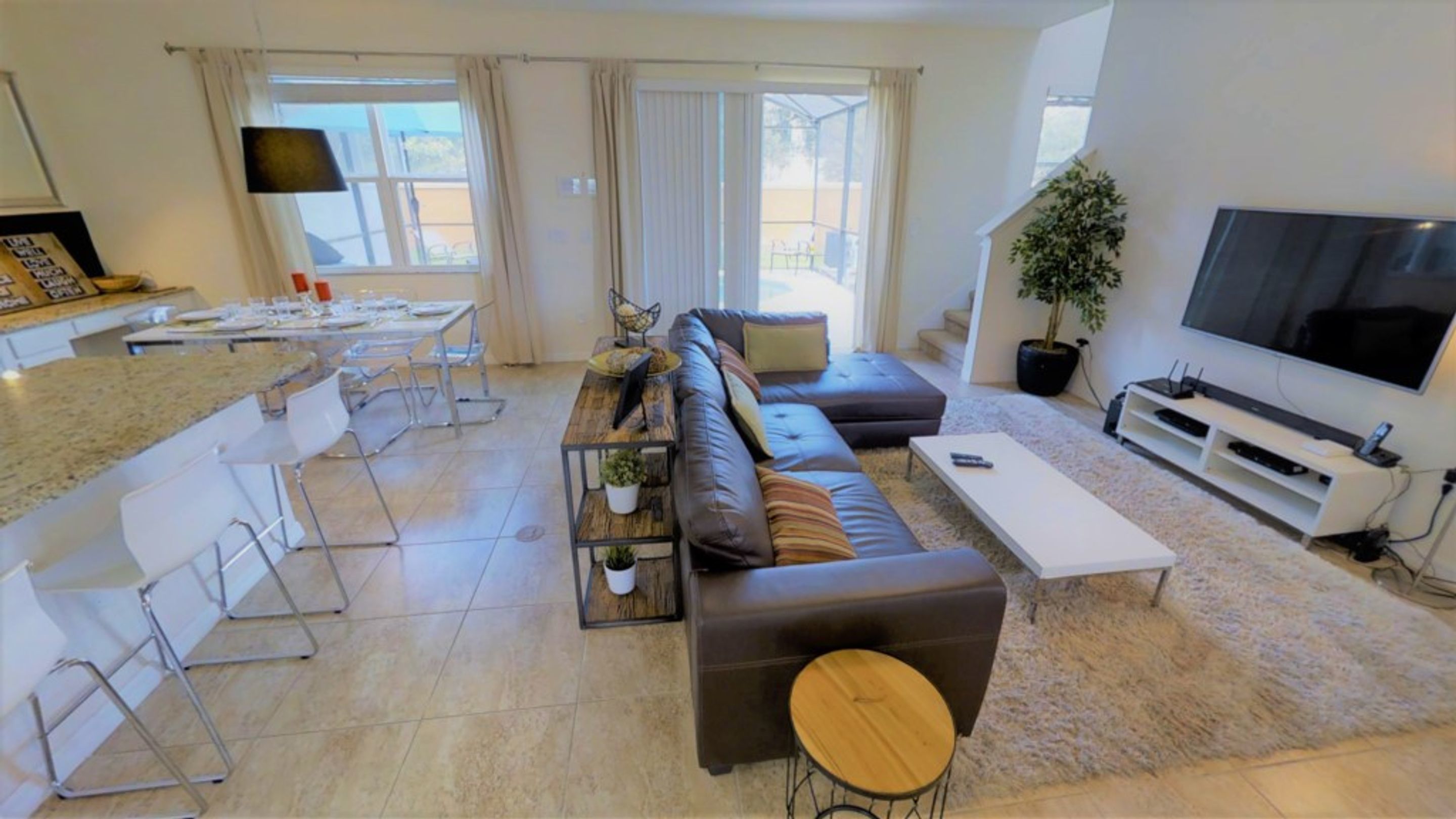 A modern living room with a sofa, coffee table, and TV. There is a dining area with chairs and a table.