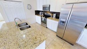 A modern kitchen with granite countertops, stainless steel appliances, and white cabinetry. - Bella Vida 850 A (Kissimmee)