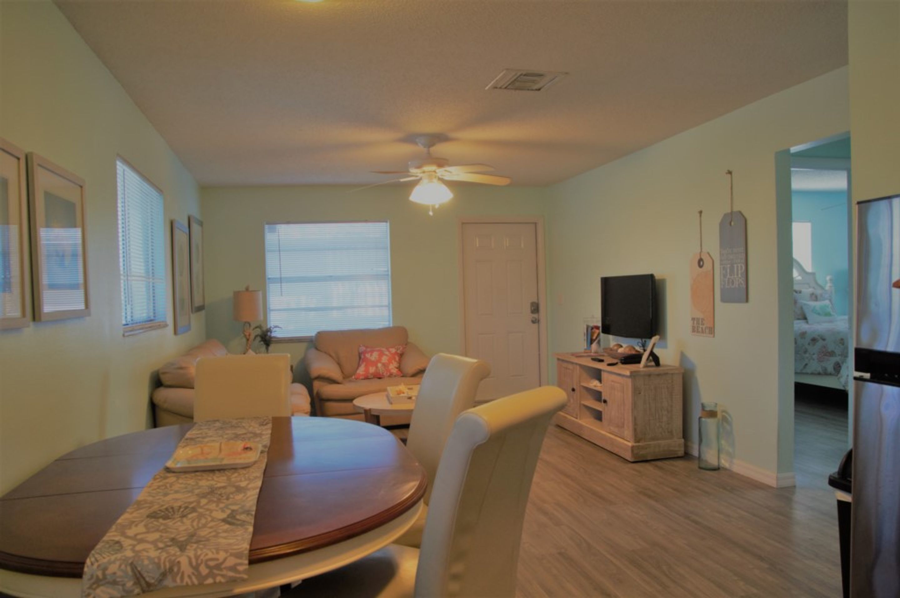 A living room with a dining table, two sofas, a TV, and a ceiling fan.